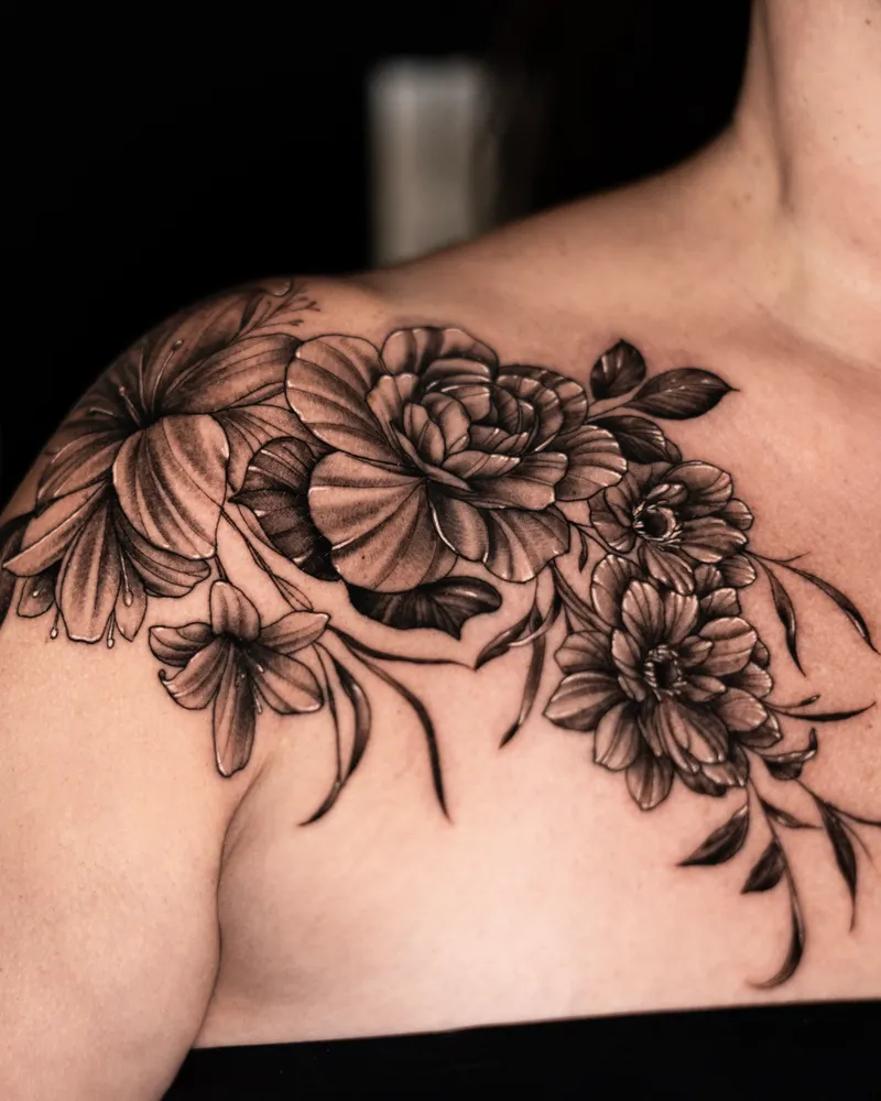 Flowers across a collarbone and shoulder: lilies, a rose and dahlias with trailing leaves
