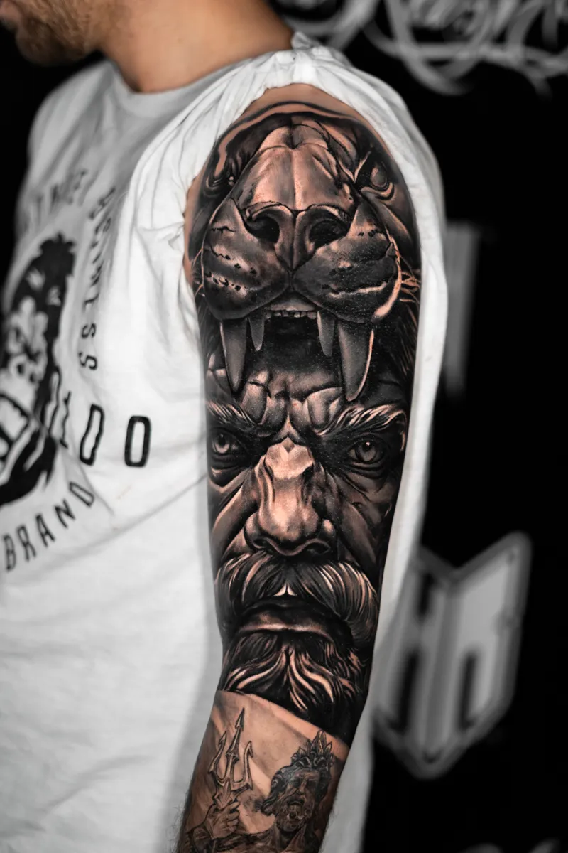 An arm sleeve: a fanged big cat's skull above a bearded face, a trident at the forearm