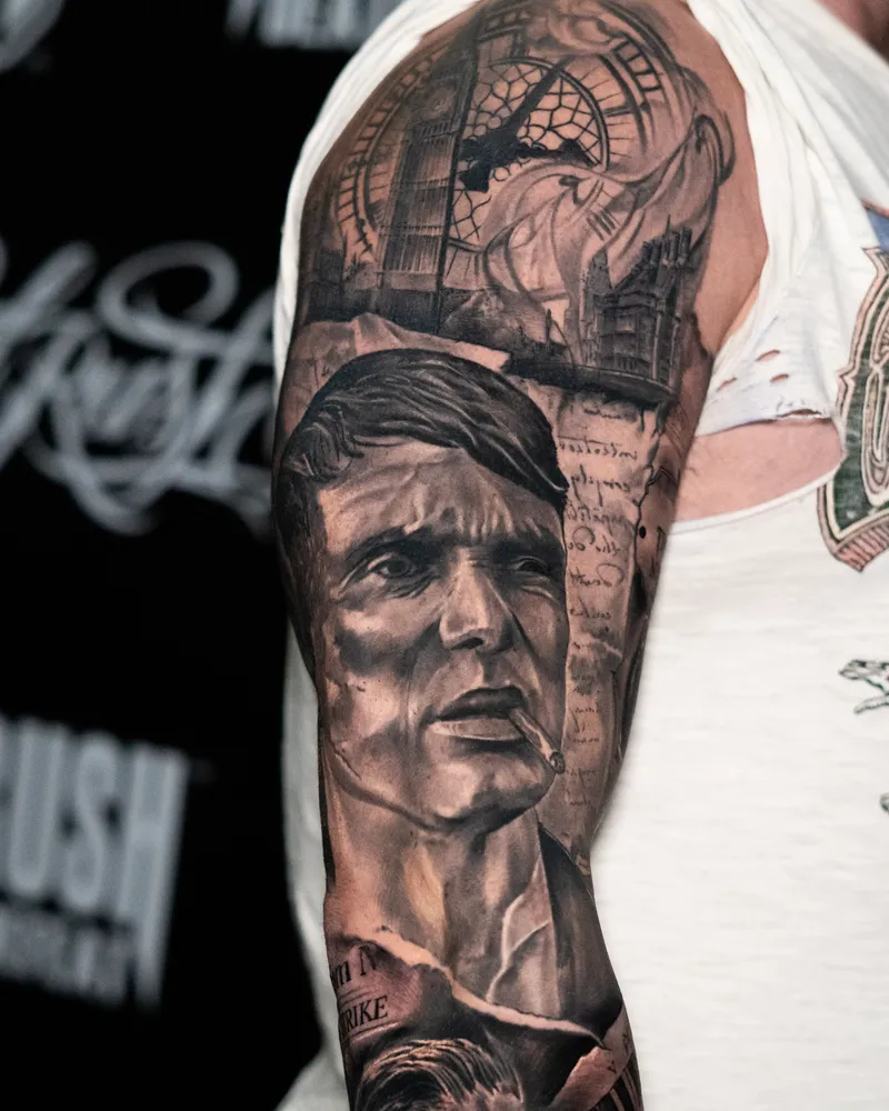 A healed arm sleeve: a man in a flat cap smoking, with a clock tower and a ruined house above him