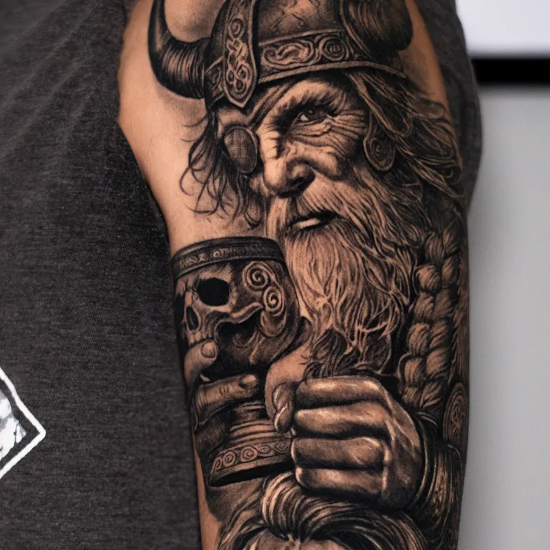 A healed upper arm: a viking in a horned helmet raising a skull cup, his beard braided